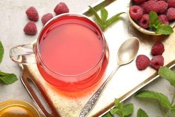 Tasty raspberry tea, berries, honey and mint on light grey table, flat lay