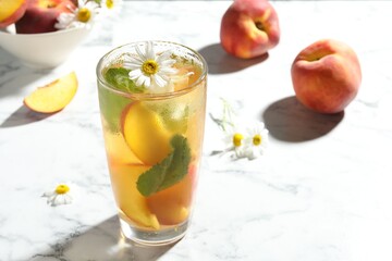 Tasty iced peach tea in glass, fresh fruits, mint and chamomile flowers on white table, space for text
