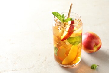 Refreshing iced peach tea with mint in glass on white table, closeup. Space for text