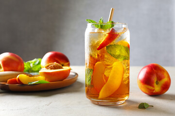 Refreshing iced peach tea with mint in glass and fresh fruits on white table, closeup