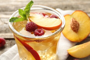 Refreshing ice tea with peach, raspberries and mint in glass on table, closeup
