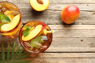 Refreshing iced peach tea in glasses and fresh fruits on wooden table, flat lay. Space for text