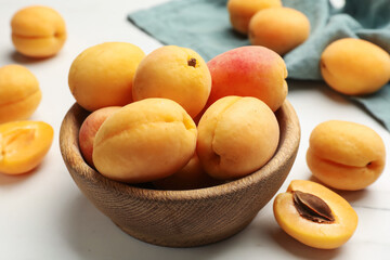 Fresh ripe apricots in bowl on white marble table, closeup