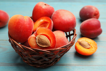 Yummy ripe apricots in wicker basket on light blue wooden table, closeup