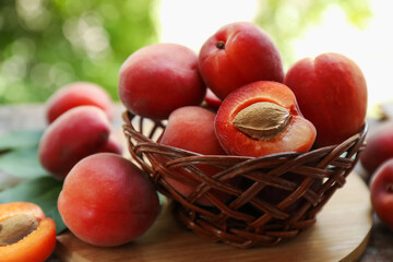 Yummy ripe apricots in wicker basket on table outdoors, closeup