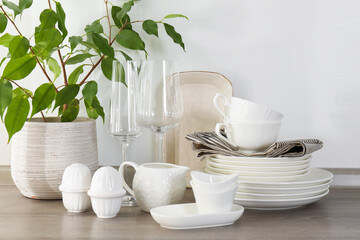 Different clean white dishware, glasses and houseplant on counter in kitchen, closeup