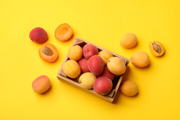Many fresh apricots and wooden crate on yellow background, flat lay