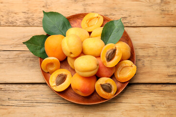Many fresh apricots and green leaves on wooden table, top view