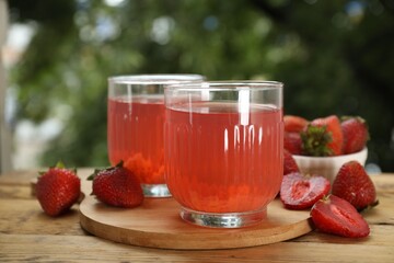 Tasty compot in glasses and fresh strawberries on wooden table outdoors, closeup