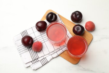 Tasty compot in glasses, plums and apricots on white marble table, flat lay