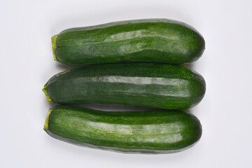 Three fresh, dark green zucchinis aligned on a plain white background