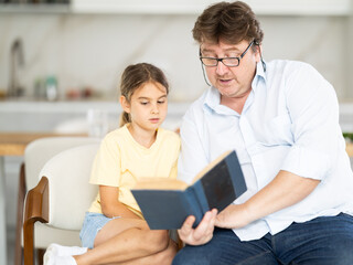 Fototapeta premium Father reads book to little cute daughter, spend leisure enjoy good life hobby and pastime at home. Fatherhood, upbringing, children development