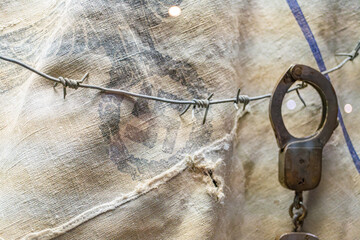 An old pair of metal handcuffs hangs from a rusted barbed wire fence against a worn, creased...