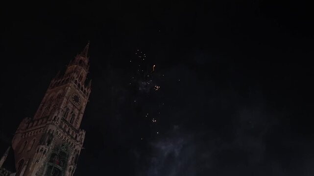 Fireworks lighting up sky behind Gothic clock tower in Munich during New Year celebration