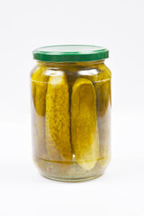 A studio shot of a glass jar filled with pickles, closed with a green lid, on a white background