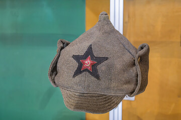 Close-up of a high-crowned, coarse fabric hat with cultural or historical significance, featuring an emblem consisting of a five-pointed star in a circle with crossed laurel branches and hammer sic