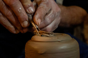 Close-up of male hands shaping clay mug on pottery wheel with sculpting tools