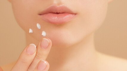 Close-up of a young woman gently applying acne spot cream for clear radiant skin. Self care, skincare, and self-confidence with targeted blemish treatment. Teenage girl, beauty tips on light backdrop