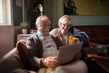 Senior couple relaxing on sofa with laptop and coffee at home