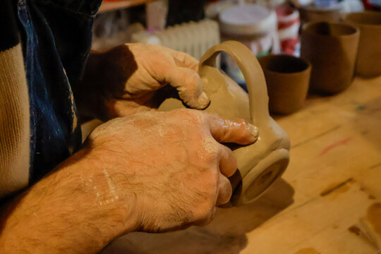 Potter's hand, the final touch as they shape and attach the handle to a cly mug