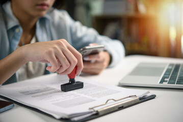 Hand of a professional woman stamping official papers on a clipboard with a laptop and phone on her desk. legal contracts, business verification, and the importance of official documentation.