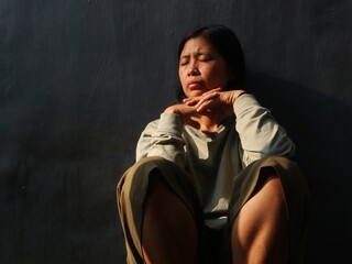 Asian sad woman sitting on gray background. Conceptual image for depression, sadness, loneliness,...