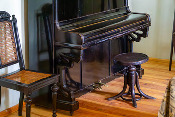 Vintage black upright piano in a wooden interior, accompanied by classic chairs with woven seats. A stylish element of traditional musical decor.