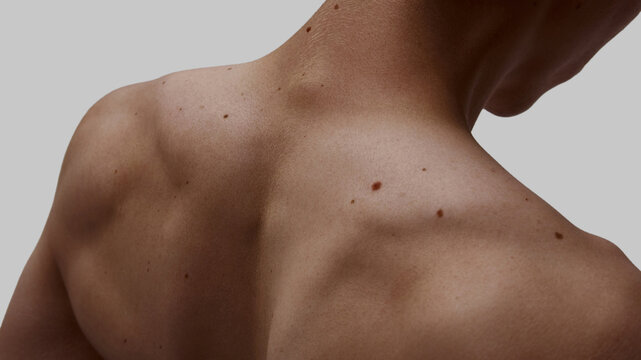 Close-up of male upper back with visible moles and muscles on neutral background. Concept of body identity, somatic health education, pain therapy, and male vulnerability.
