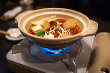 Japanese nabe hot pot (Nabemono) with mushrooms, tofu, radish, and vegetables simmering over a gas flame in a ceramic pot