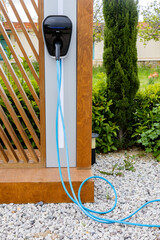 Electric car charging station with blue cable plugged into the socket in the garden