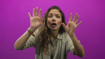 Woman expressing emotion with hands raised against vivid pink background conveys surprise and...