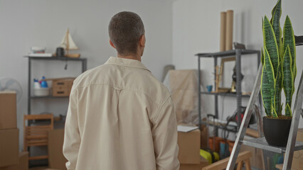 Man standing in living room of new apartment surrounded by boxes and shelves while smiling and relaxed
