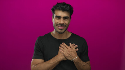 Obraz premium Man wearing black shirt clutching chest with both hands in magenta studio portrait under soft lighting; gratitude.