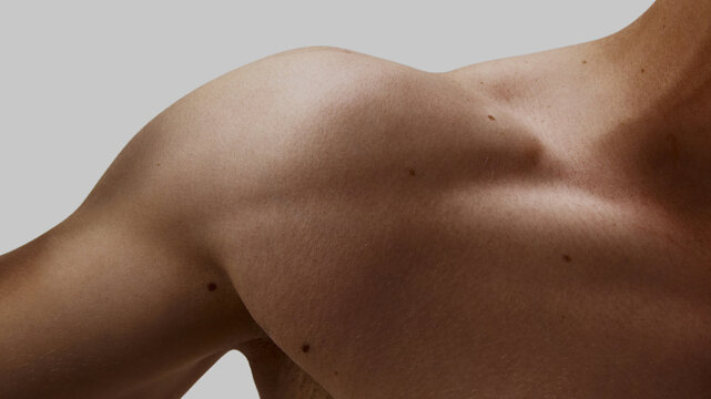 Male shoulder and collarbone detail under soft light with clean background. Concept of osteopathy branding, men body acceptance, fashion and fitness hybrids, and emotional resilience design.