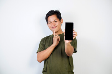 Naklejka premium Young Asian man smiling while pointing to and holding a smartphone