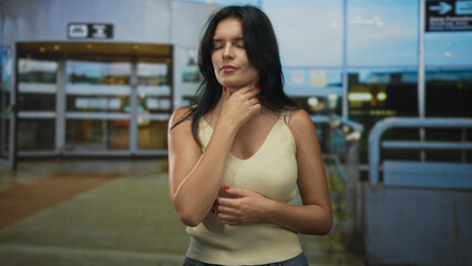 Woman clutching chest with pained expression and hand on stomach at airport terminal experiencing heartattack; anxiety uncertainty.
