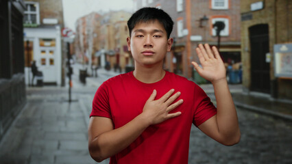 Young man in red shirt gestures on a city street, expressing emotion, against a backdrop of urban architecture and cobblestone pavement, capturing a vibrant outdoor scene.