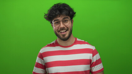 Obraz premium Young man with glasses and beard wearing red striped shirt smiling against vibrant green background exuding happiness and casual style.