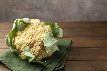 Fresh cauliflower with green leaves on wooden table, closeup. Space for text