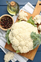 Raw cauliflower, peppercorns and oil on blue wooden table, flat lay