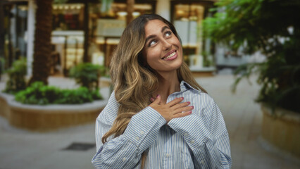 Fototapeta premium Young blonde woman clutching chest in plaza; gratitude happiness.