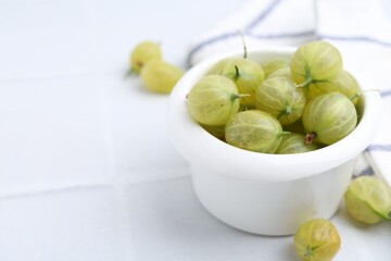 Fresh green gooseberries in bowl on white table, closeup. Space for text