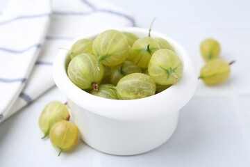 Fresh green gooseberries in bowl on white table, closeup