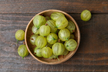 Fresh green gooseberries in bowl on wooden table, top view