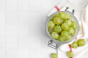 Fresh green gooseberries in jar on white tiled table, top view. Space for text