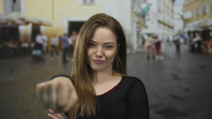 Fototapeta premium Young woman extends fist toward camera in a crowded busy city street; empowerment solidarity confidence activism.