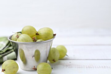 Ripe green gooseberries in bowl on white wooden table, closeup. Space for text