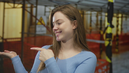 Fototapeta premium Young caucasian woman in blue sweater makes ok sign with hand in front of a building construction site; approval.