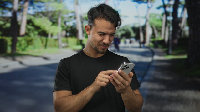 Young hispanic man smiling while using smartphone on a sunny street captures urban outdoor lifestyle in a bustling city environment.