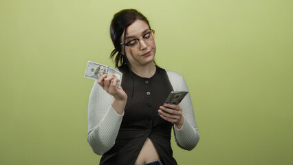 Woman counting us dollars with focused expression against yellow background, wearing glasses and...